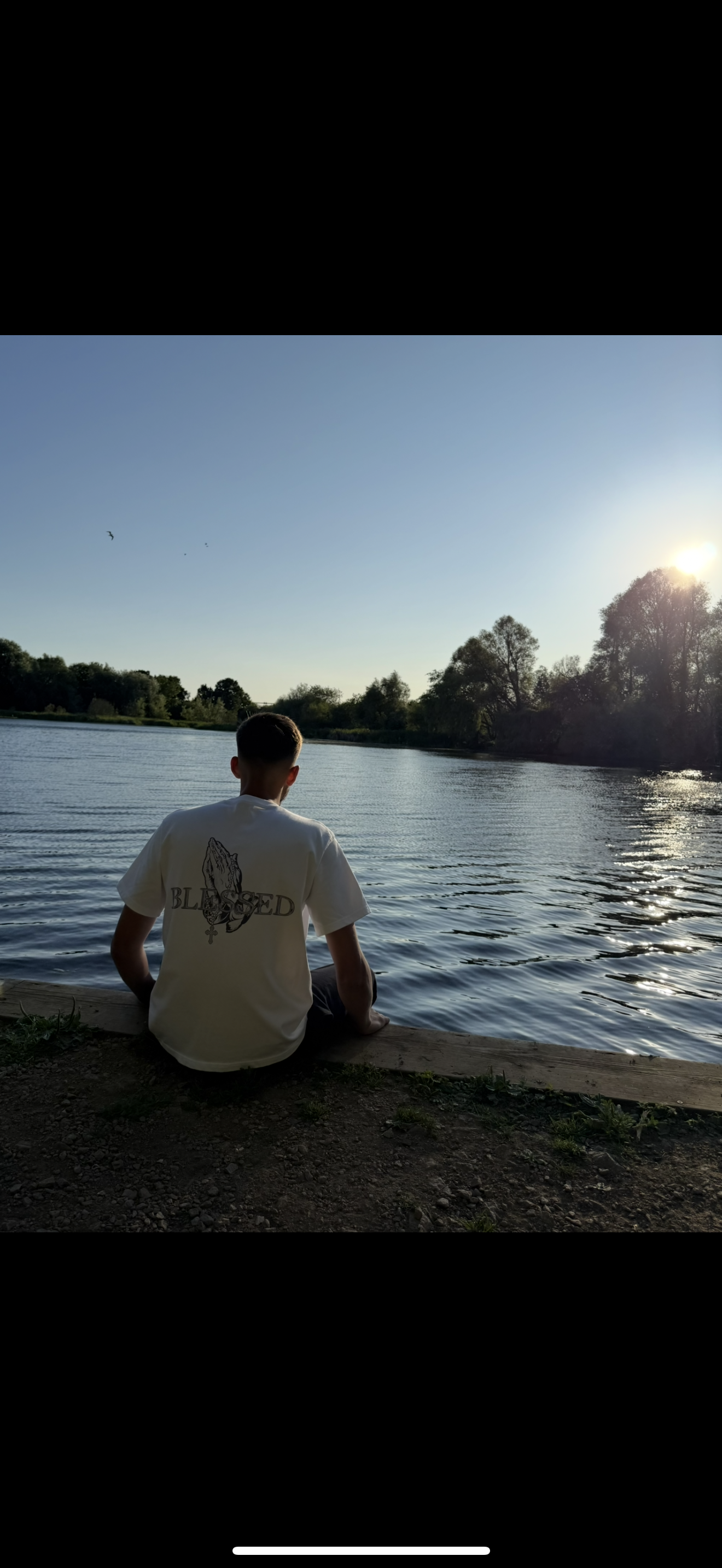 Person sitting by a lake with trees and Blessed writing on a t-shirt